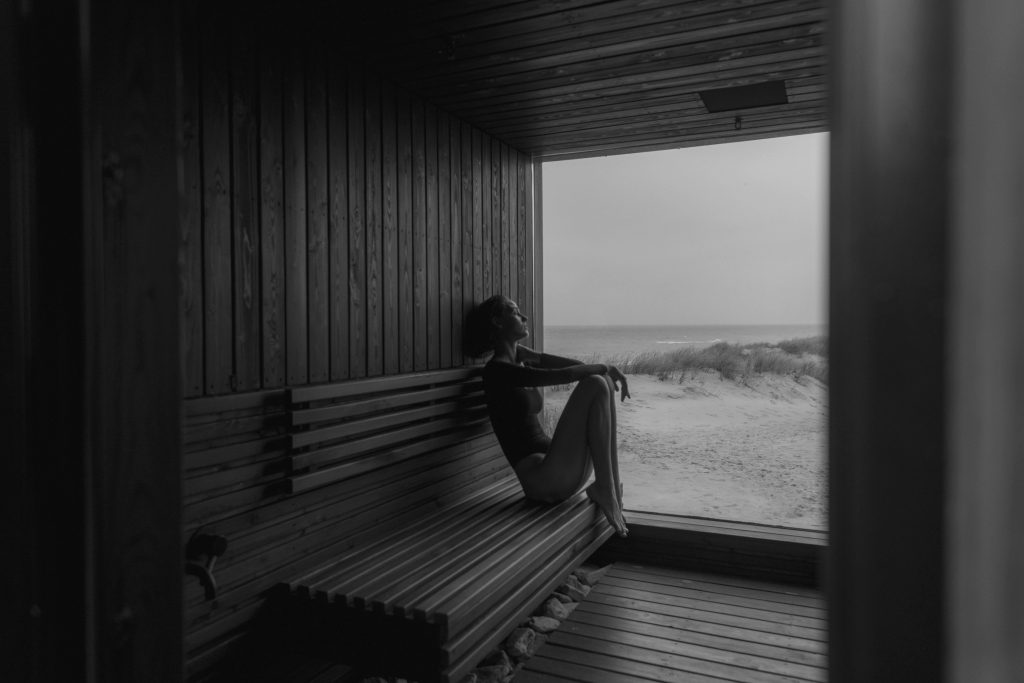 Black and white image of a woman sitting in a beachfront sauna, gazing at the sea.